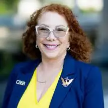 Smiling woman with curly red hair, glasses, and a CPHA blue blazer, pictured outdoors.